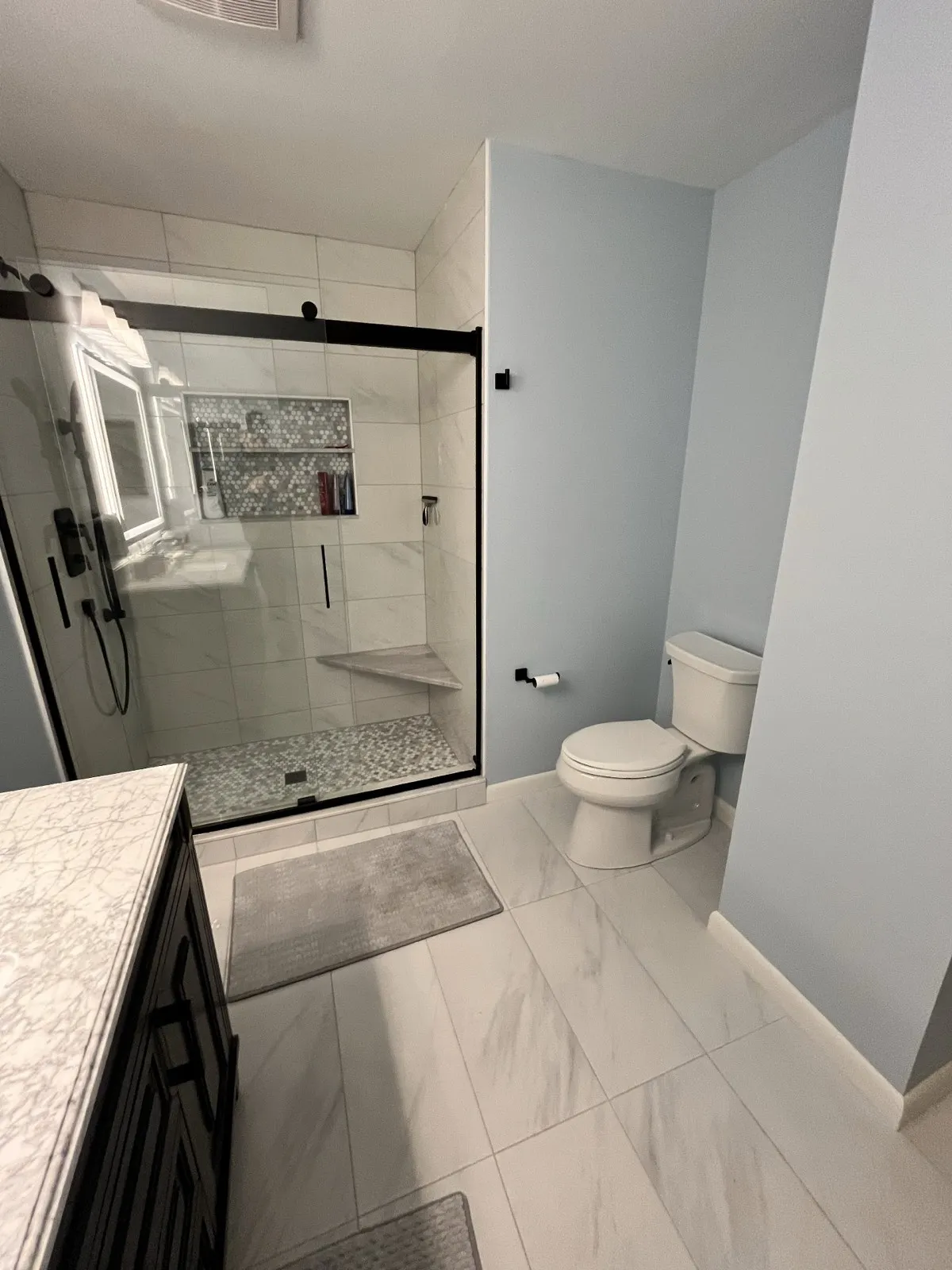 Finished bathroom with a glass shower and white tile floor, by Kubat Construction