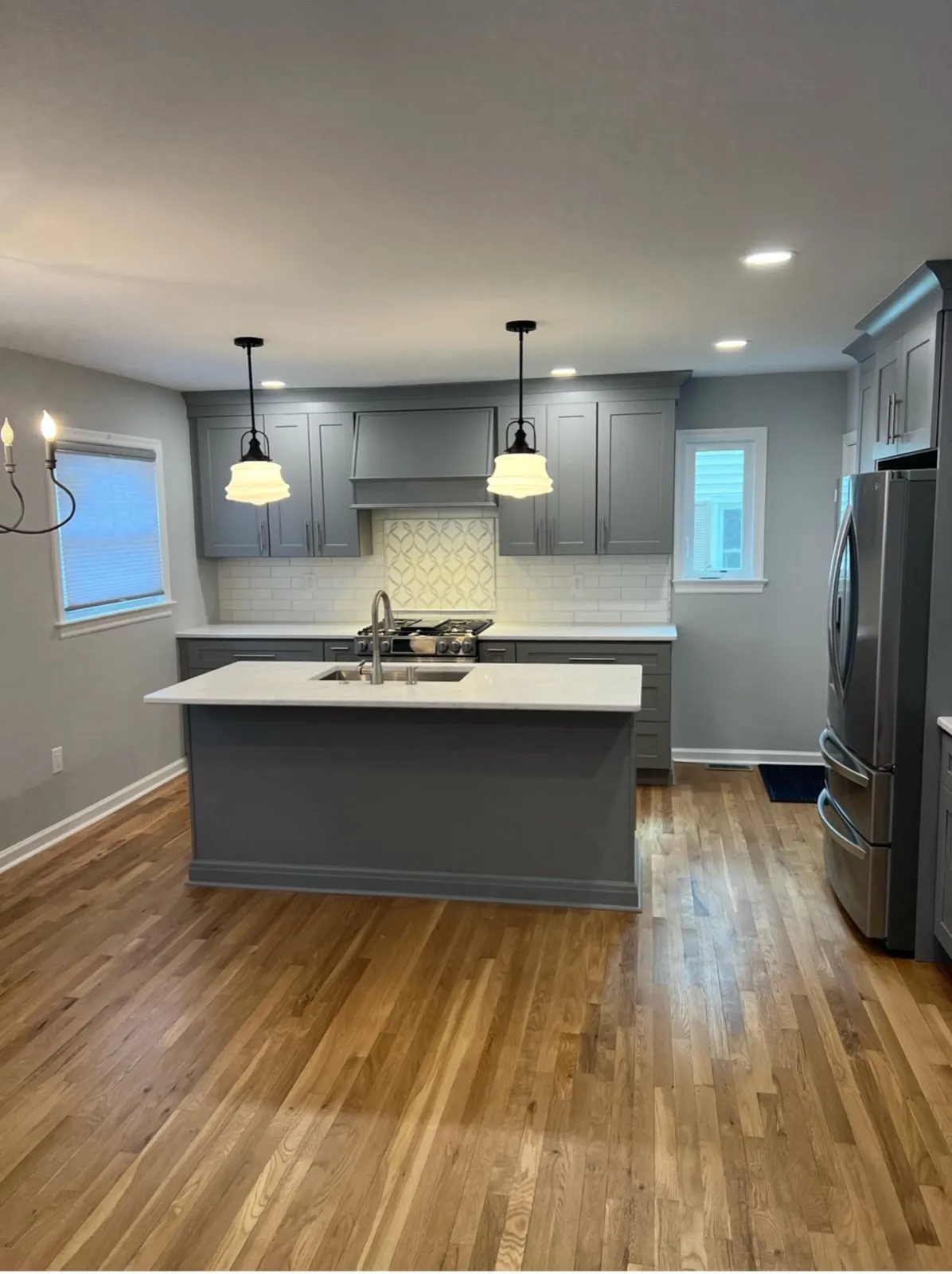 Kitchen with a gray island, pendant lights and wood floors, by Kubat Construction